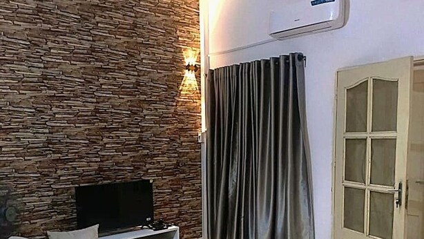 Ein Wohnzimmer mit Steinwand, Flachbildfernseher, beiges Sofa und einer Glastür.