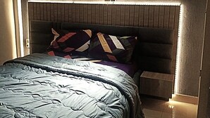 Ein Schlafzimmer mit einem Bett, einem Kopfteil mit integrierter Beleuchtung und einem Nachttisch.