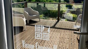 A wooden deck with outdoor seating and a view of greenery and buildings in the distance.