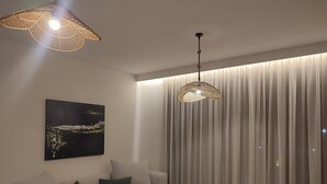A modern living room with a sofa, two small tables, a hanging light fixture, and a large window with curtains. - Darion Townhouse (Nikiti)