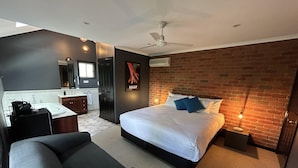 Un dormitorio moderno con una cama grande, un sofá gris oscuro, un escritorio pequeño y una pared de ladrillo.
