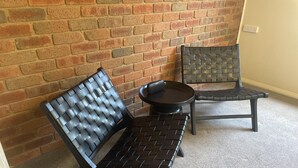 Un rincón con un muro de ladrillo, una mesa redonda y dos sillas de metal negro.