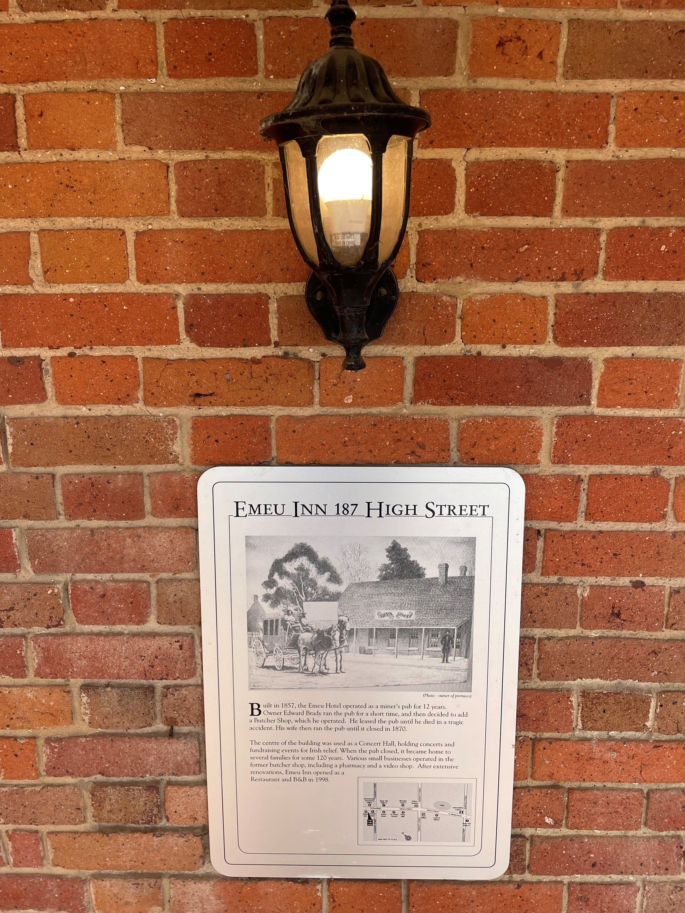A historical plaque on a brick wall with a vintage street lamp above it.