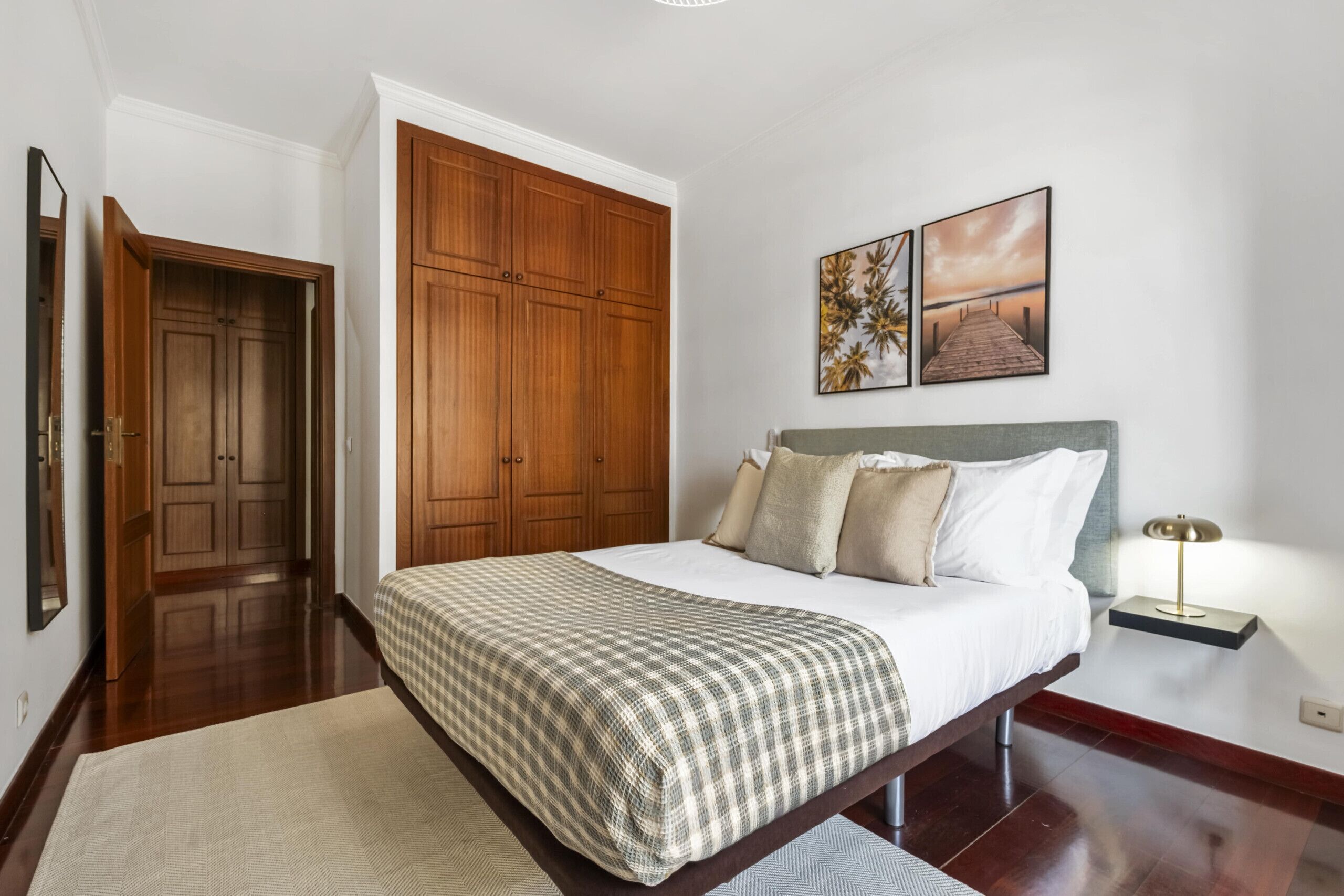 A bedroom with a large bed, wooden wardrobe, and two wall-mounted paintings.