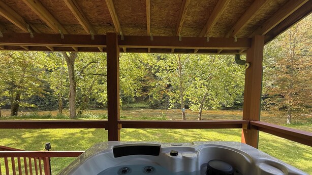 Una vasca idromassaggio sotto un gazebo di legno con vista su una zona erbosa e alberi.