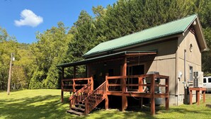 Una baita rustica con tetto verde, veranda in legno e una scala che conduce all'ingresso.