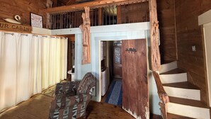 Interno di una baita con una scala in legno, un divano e un cartello con la scritta 'OUR CABIN'.