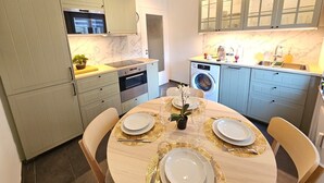 A modern kitchen with a built-in oven, microwave, and washing machine. There is a dining table set with plates and cutlery. - Ideal city stay 1BR near train station (Luxembourg City)