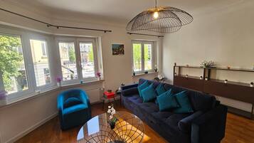A modern living room with a dark blue sofa, a glass coffee table, and a unique wireframe pendant light.