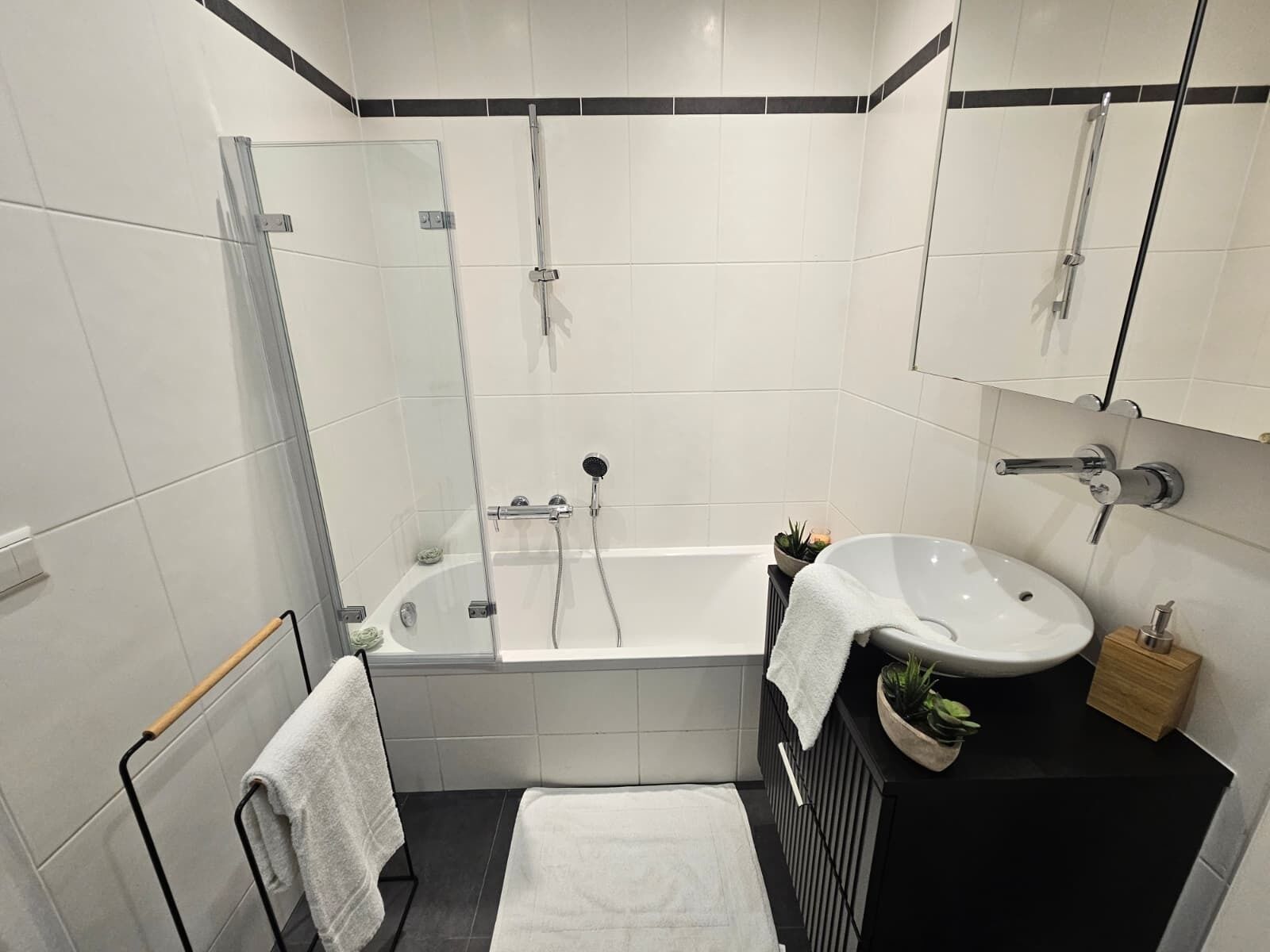 Ein modernes Badezimmer mit einer Duschkabine, einer weißen Badewanne, einem Waschbecken mit Spiegel und einem Handtuchhalter.