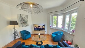 A modern living room with a sofa, two armchairs, a coffee table, a TV, and a pendant light. - Ideal city stay 1BR near train station (Luxembourg City)