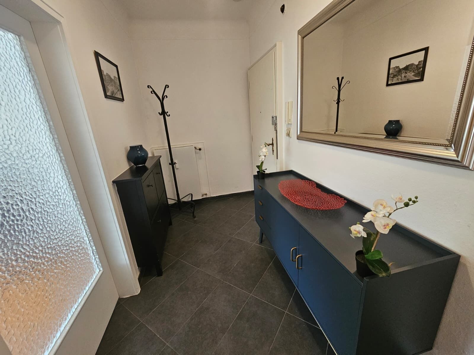 Een badkamer met een donkerblauwe wastafel, een witte radiator, een zwarte kast en een spiegel met een afbeelding in de lijst.