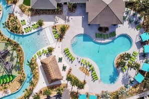 Vista aérea de um resort com uma grande piscina central, várias piscinas menores e espreguiçadeiras dispostas ao redor das piscinas.