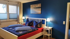 Une chambre à coucher avec un lit, deux tables de chevet, une fenêtre avec des stores et un tableau au mur.