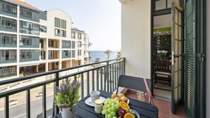 En balkong med ett bord dukat för frukost, med utsikt över en byggnad och havet.