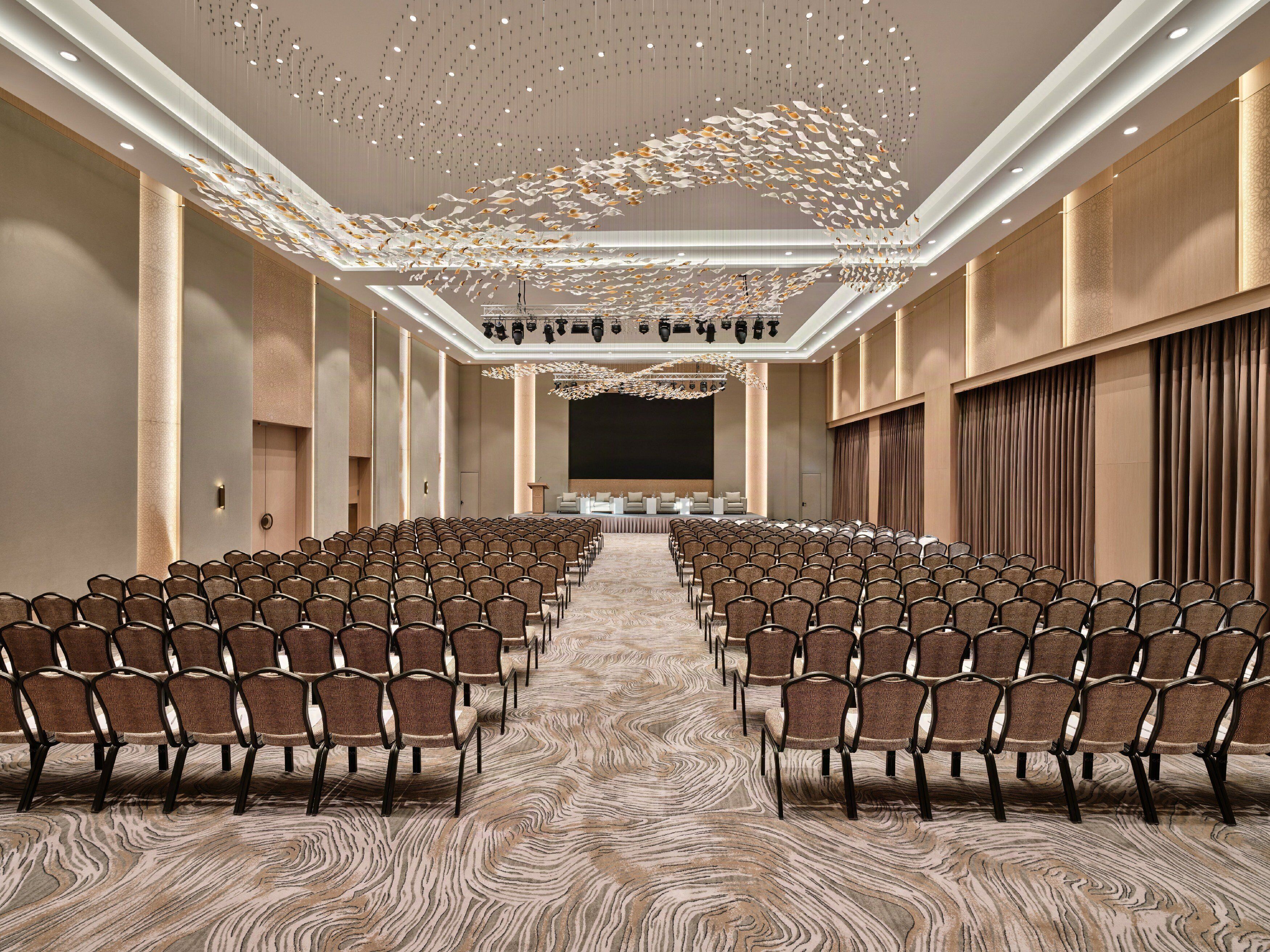 Un salón de conferencias con hileras de sillas, un escenario y una alfombra estampada.