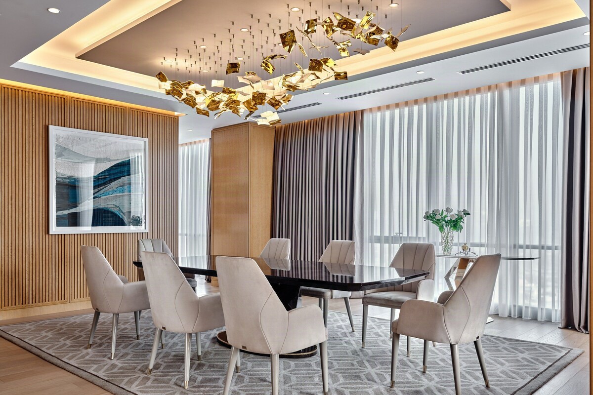 A modern conference room with a round table, six chairs, a large abstract painting, and a decorative ceiling light fixture.