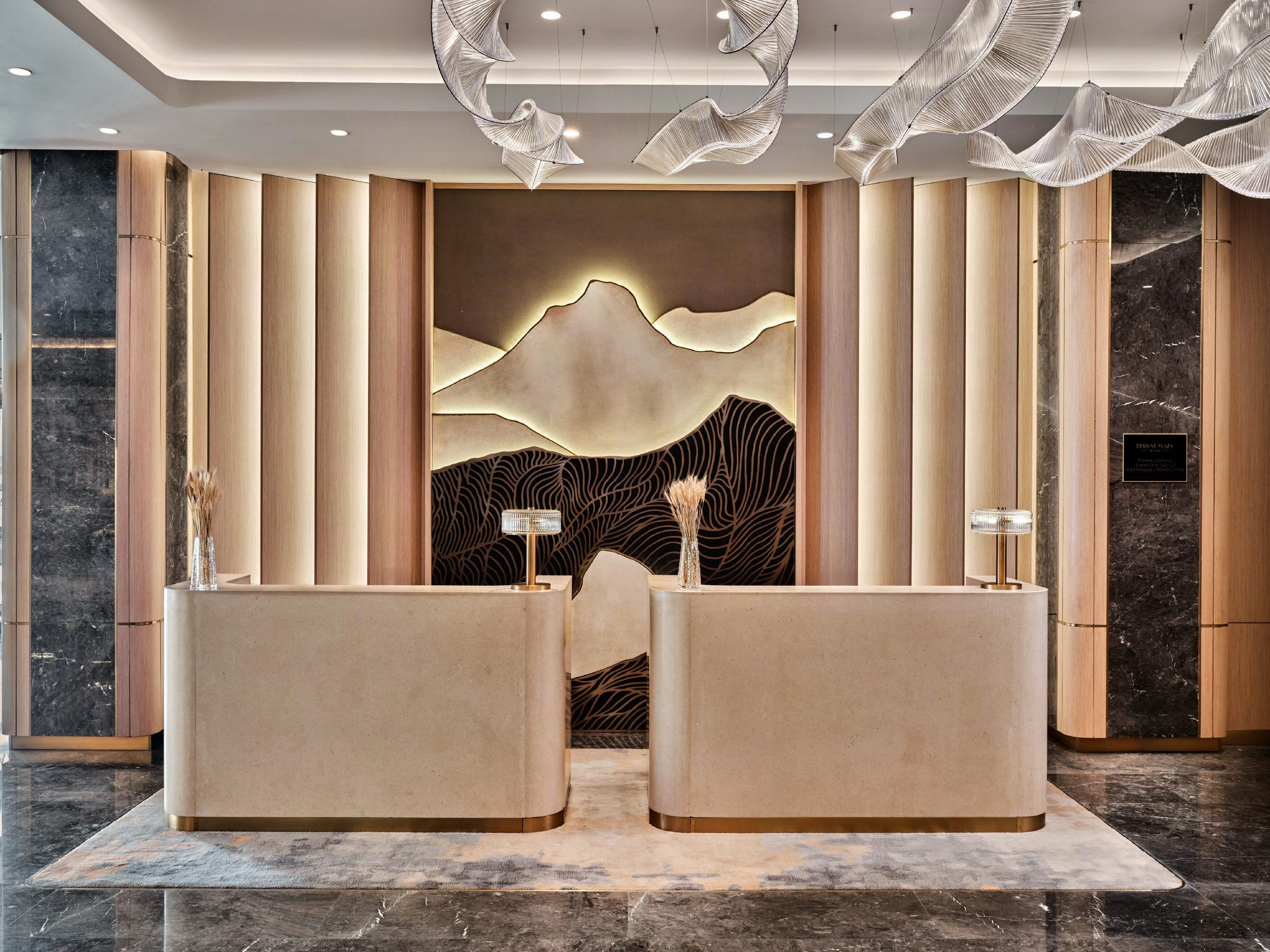 A reception area with two reception desks, a wall with a mountain and wave design, and a marble floor.