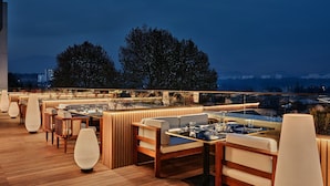An outdoor dining area with wooden flooring, cushioned seating, and modern lighting. - Crowne Plaza Dushanbe by IHG (Dushanbe)