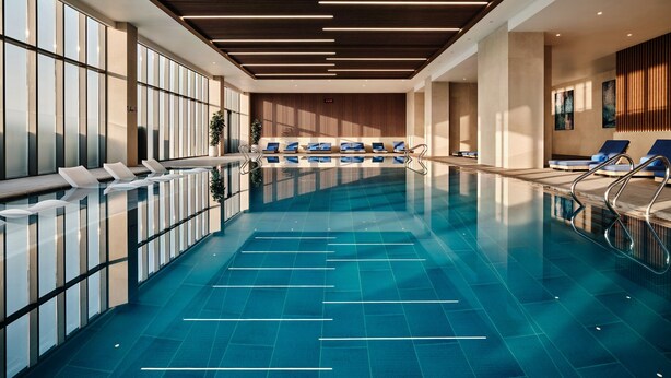 A modern indoor swimming pool with clear water, lounge chairs, and a wooden ceiling. - Crowne Plaza Dushanbe by IHG (Dushanbe)