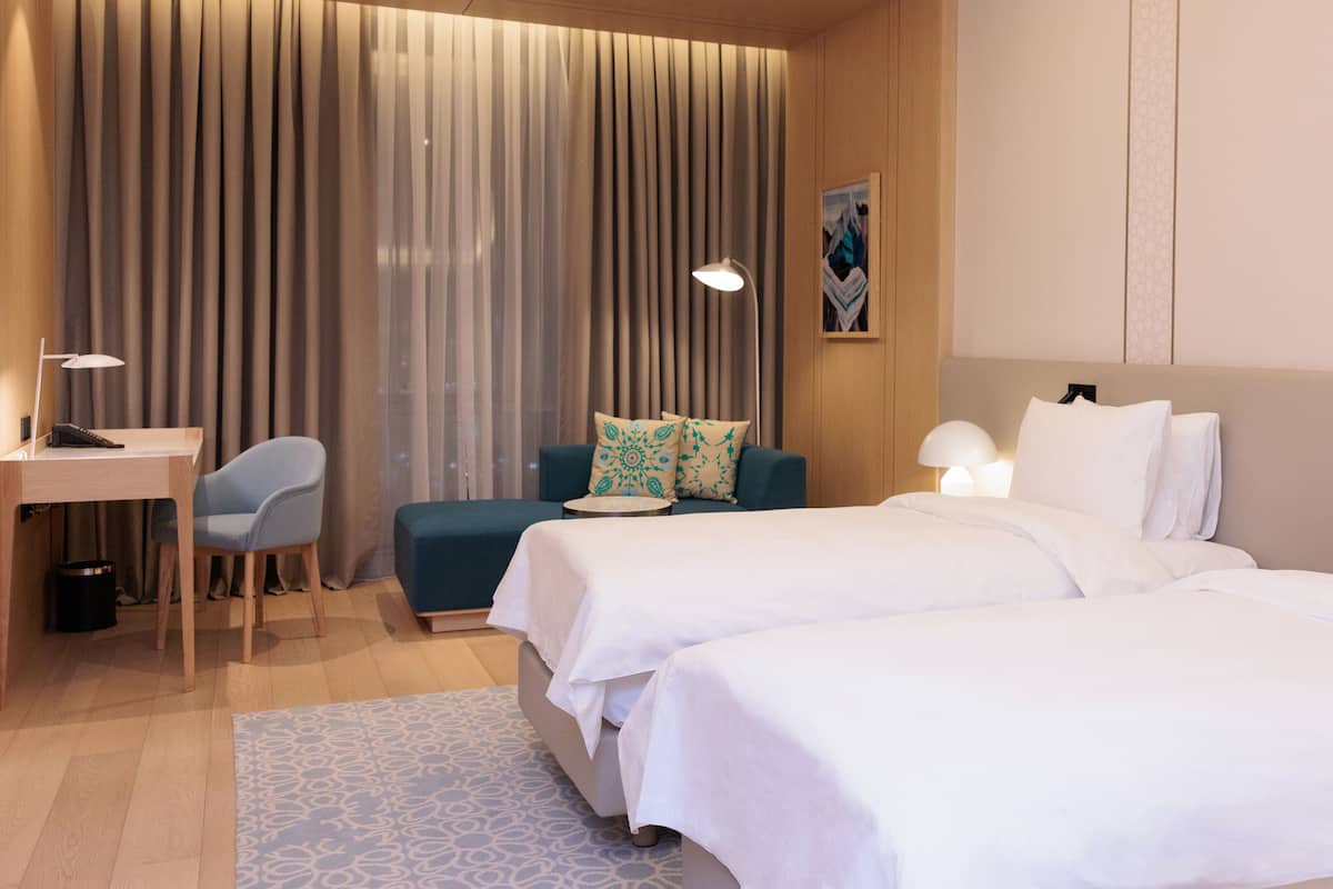 A hotel room with two beds, a desk, a chair, and a small table.