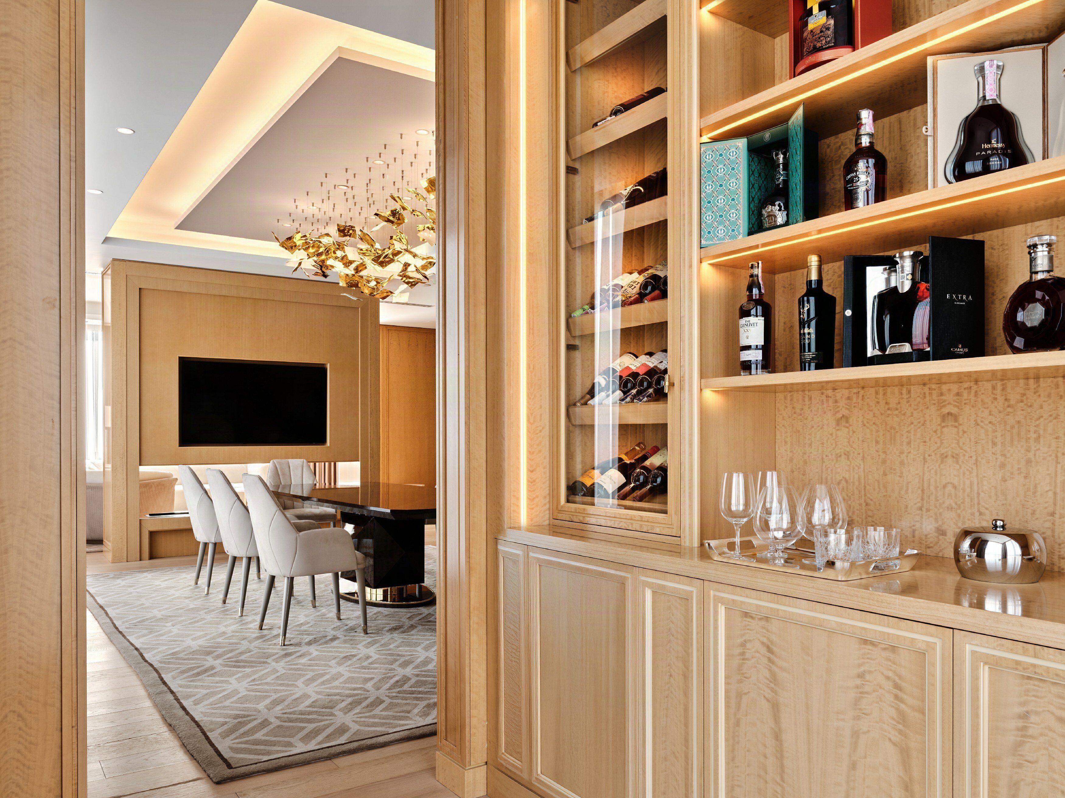 A modern interior with a wooden cabinet displaying various bottles and glasses, a dining area with a TV, and a chandelier.