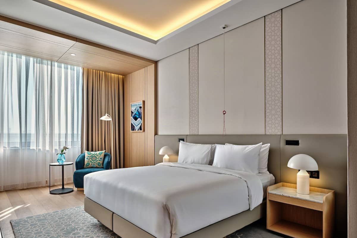 A modern hotel room with a large bed, bedside tables, a desk, and a chair.