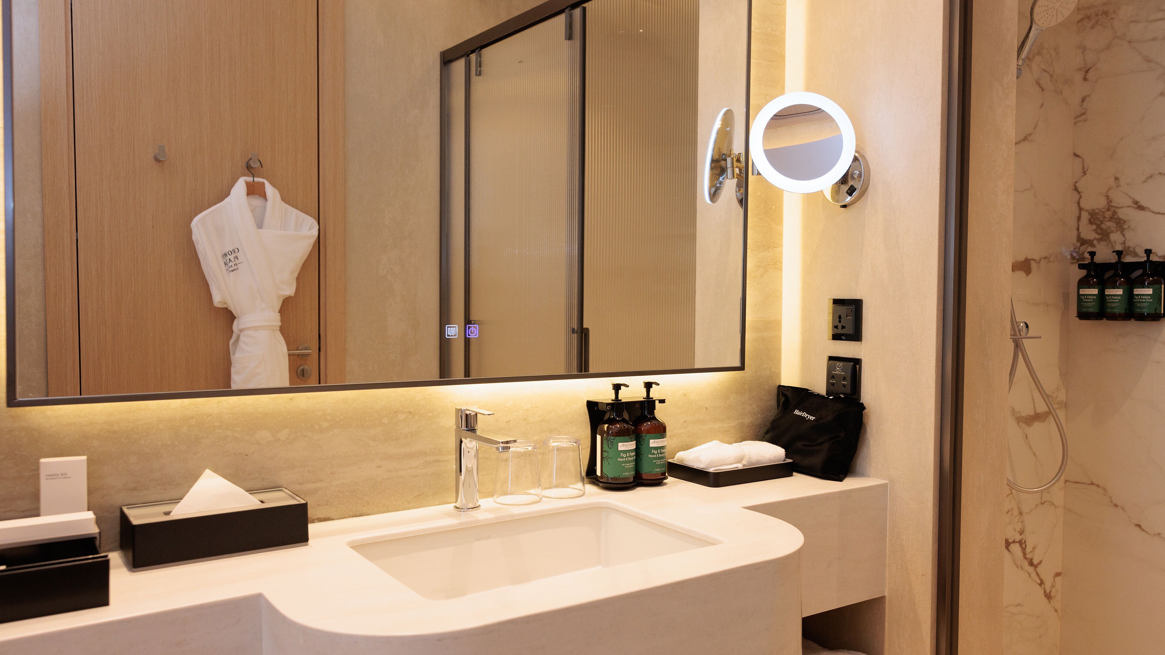 A modern bathroom with a large mirror, a sink, and a robe hanging on a door.
