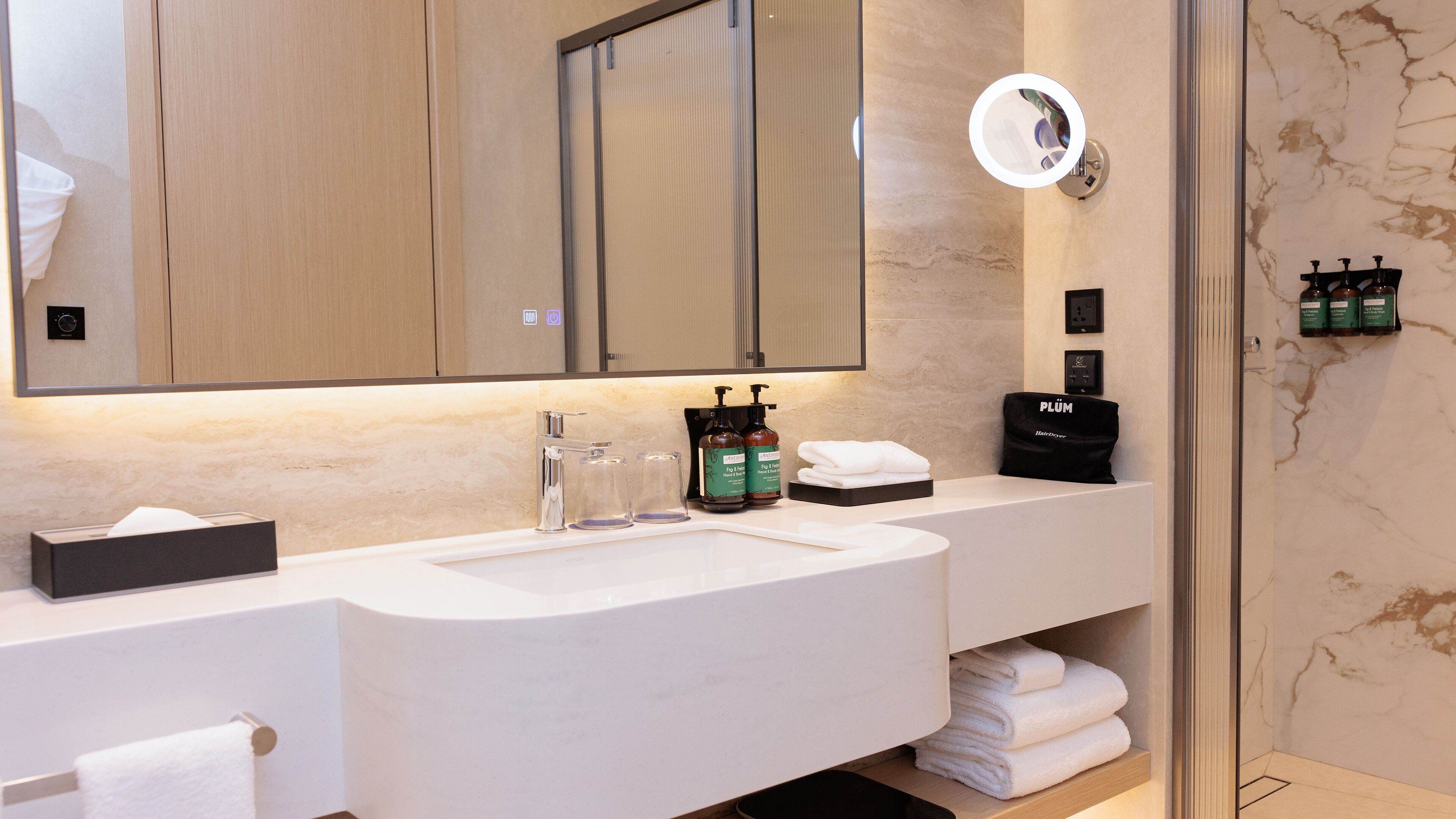 A modern bathroom with a large mirror, a sink, and a vanity. There are toiletries and a towel rack visible.