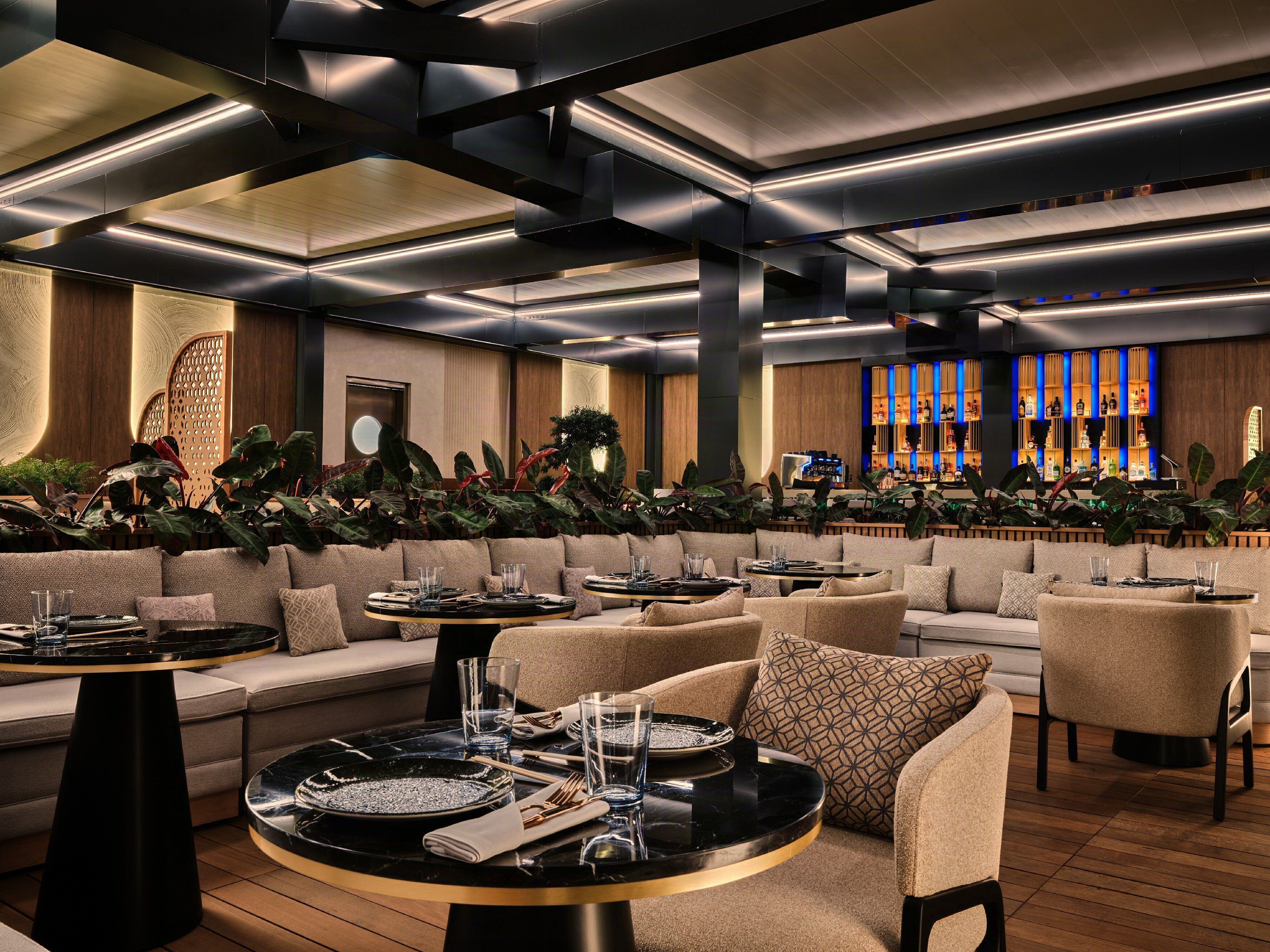 Un área de lounge moderna con sofás, mesas redondas y una barra con estantes iluminados.