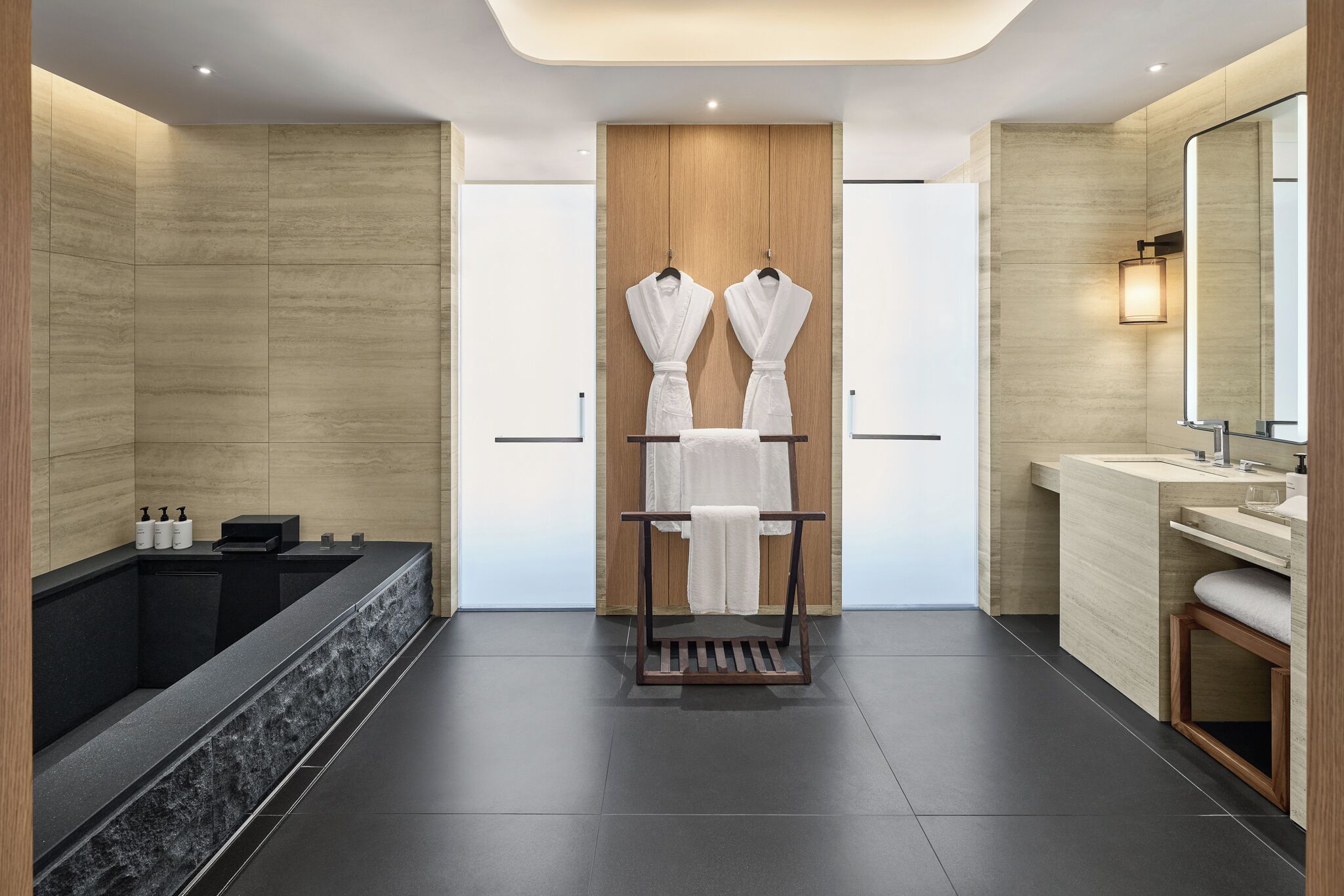 A modern bathroom with a large bathtub, a wooden vanity, and two robes hanging on a rack.