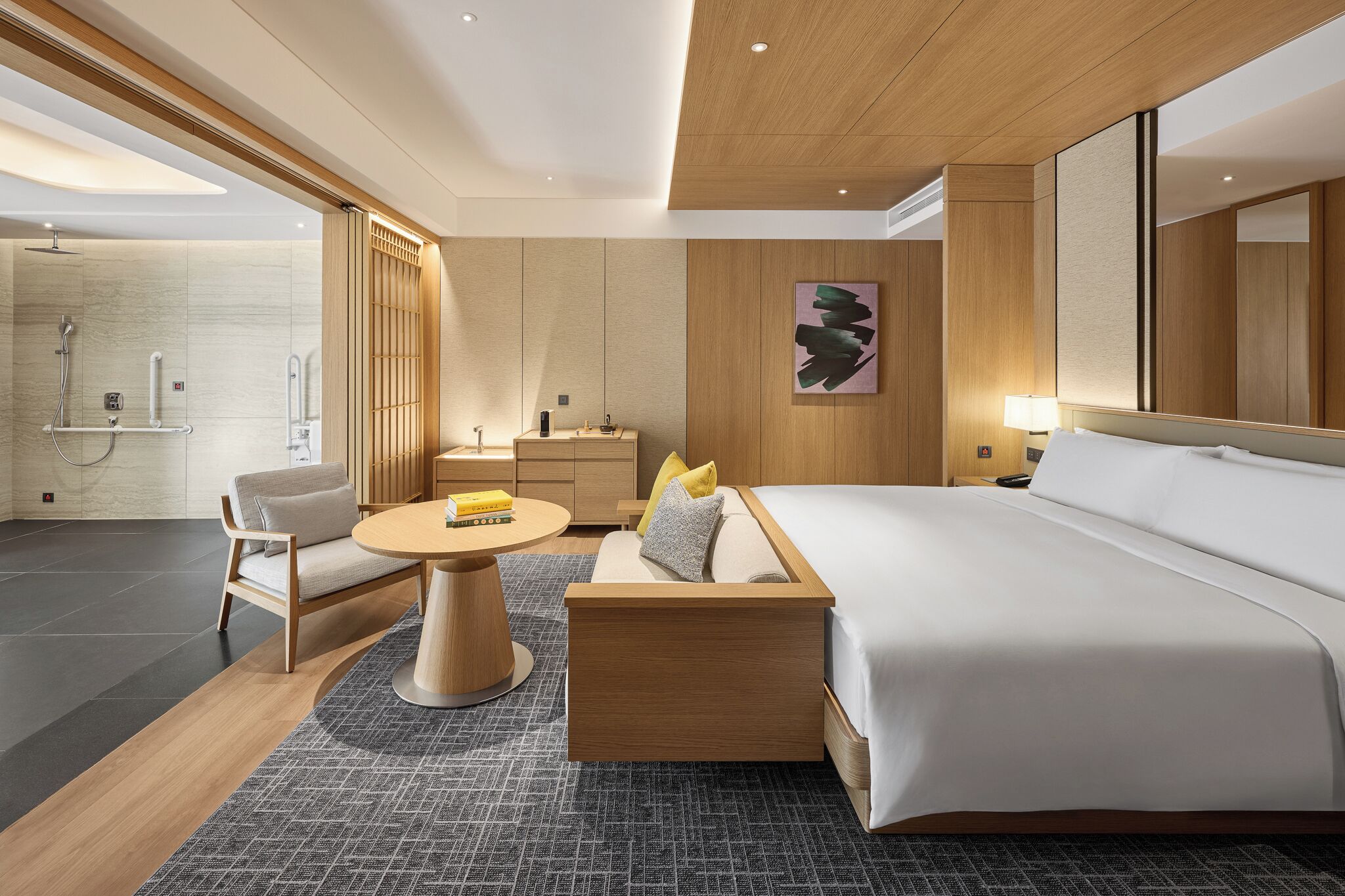 Une chambre d’hôtel moderne dotée d’un grand lit, d’un coin salon avec une table, d’une salle de bain avec douche et d’un grand miroir.