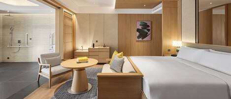 Une chambre d’hôtel moderne dotée d’un grand lit, d’un coin salon avec une table, d’une salle de bain avec douche et d’un grand miroir.
