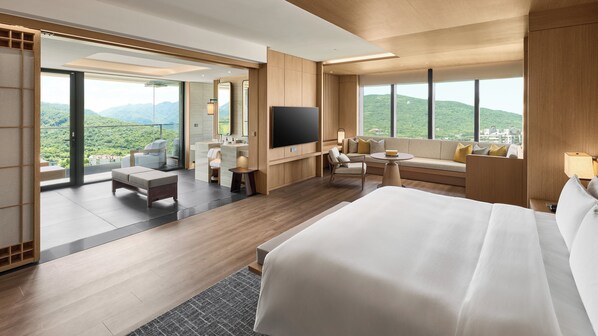 Camera d'albergo con un letto grande, una televisione, un divano, una scrivania e un balcone con vista sulle montagne.