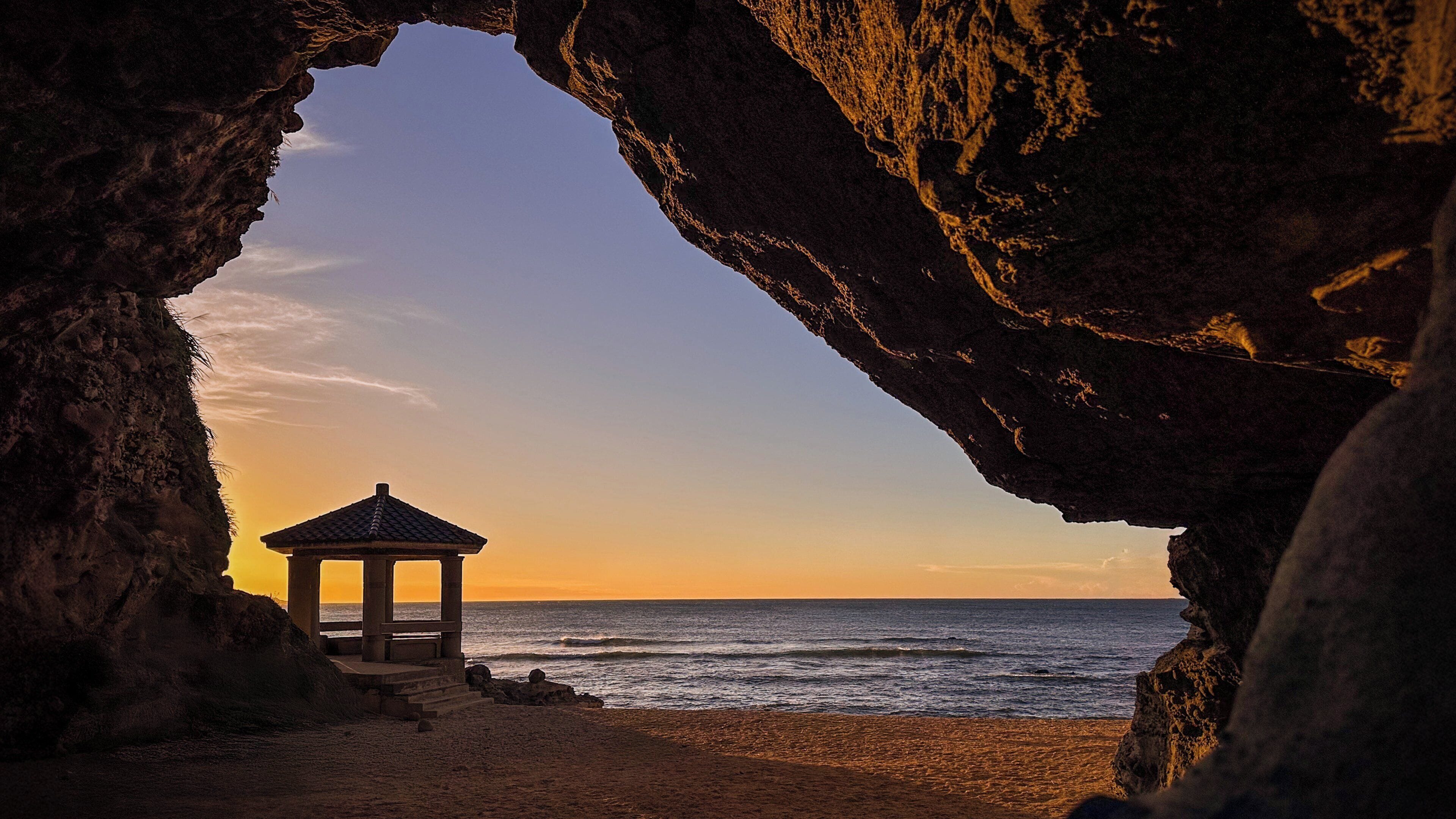 A gazebo on a beach framed by a natural rock arch.