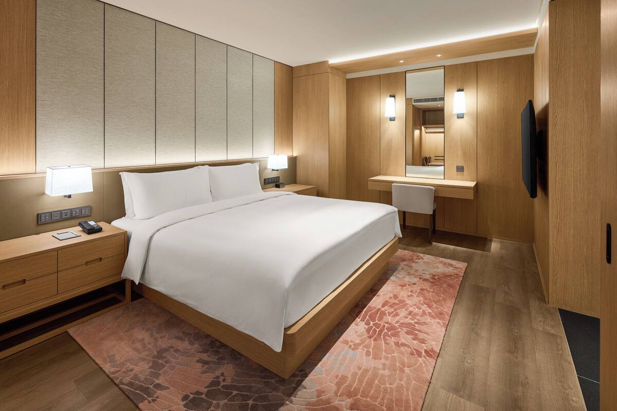 Une chambre d’hôtel moderne avec un grand lit, des tables de chevet, un bureau et un miroir.