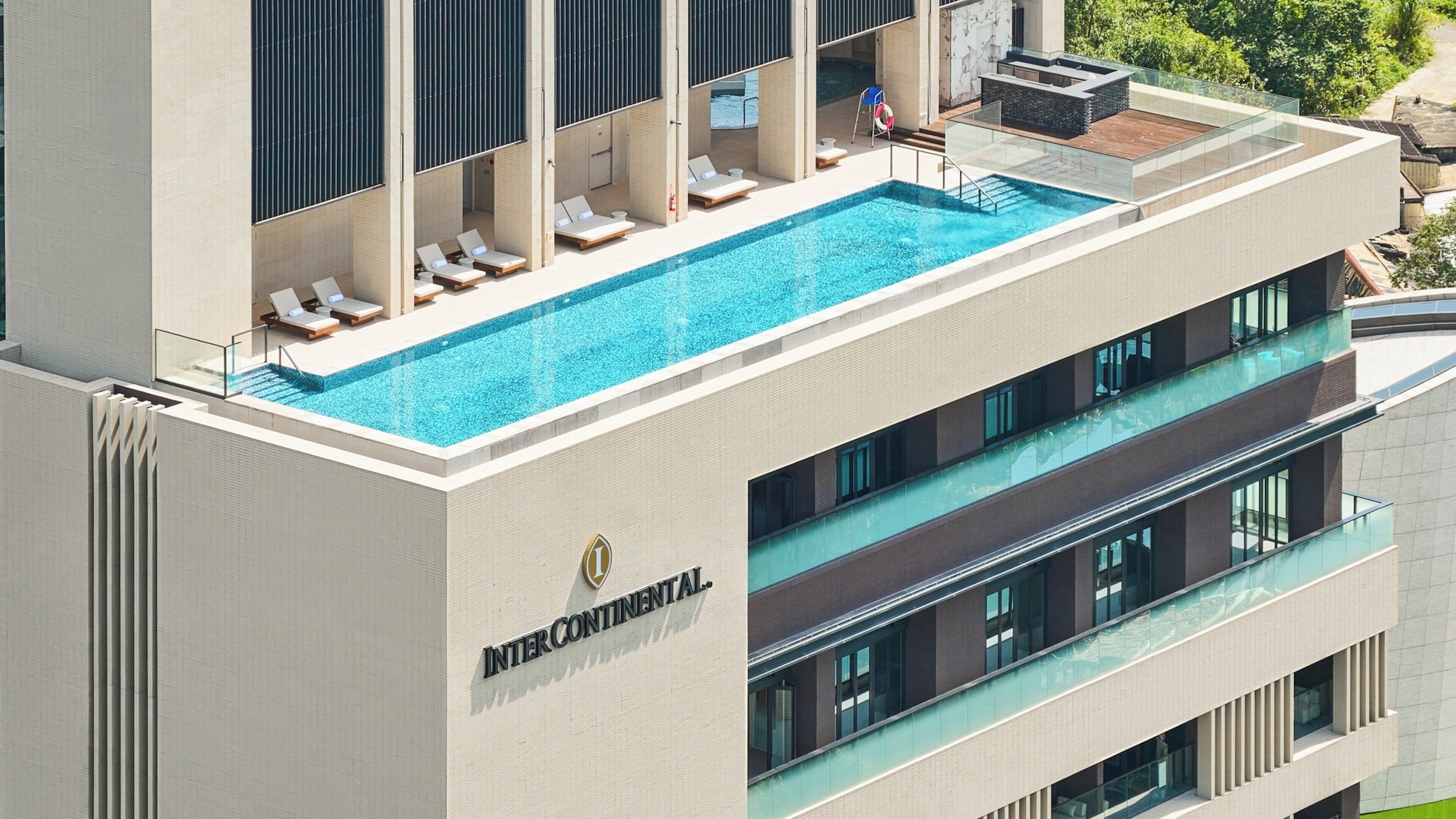 A hotel with a rooftop pool, multiple balconies, and a clear view of the surrounding area.