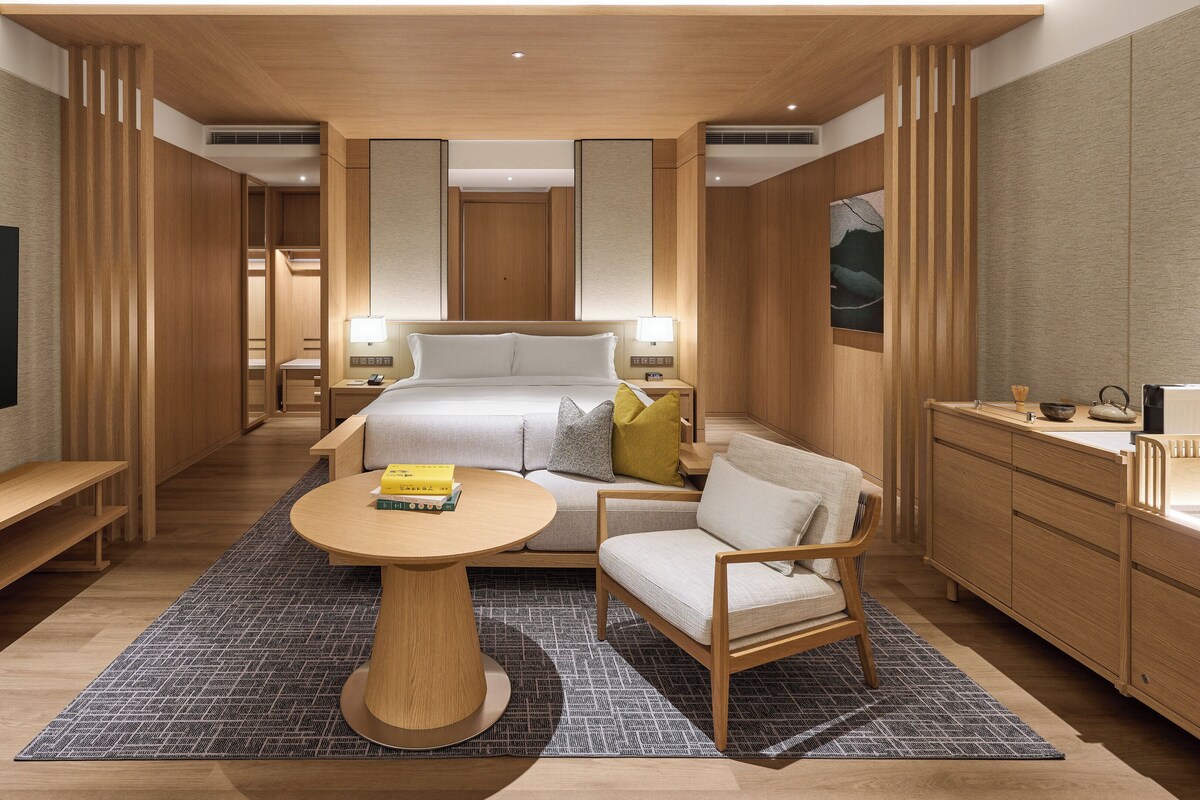 Ein modernes Hotelzimmer mit einem großen Bett, einer Sitzecke mit Tisch, einem Fernseher und einer Minibar.