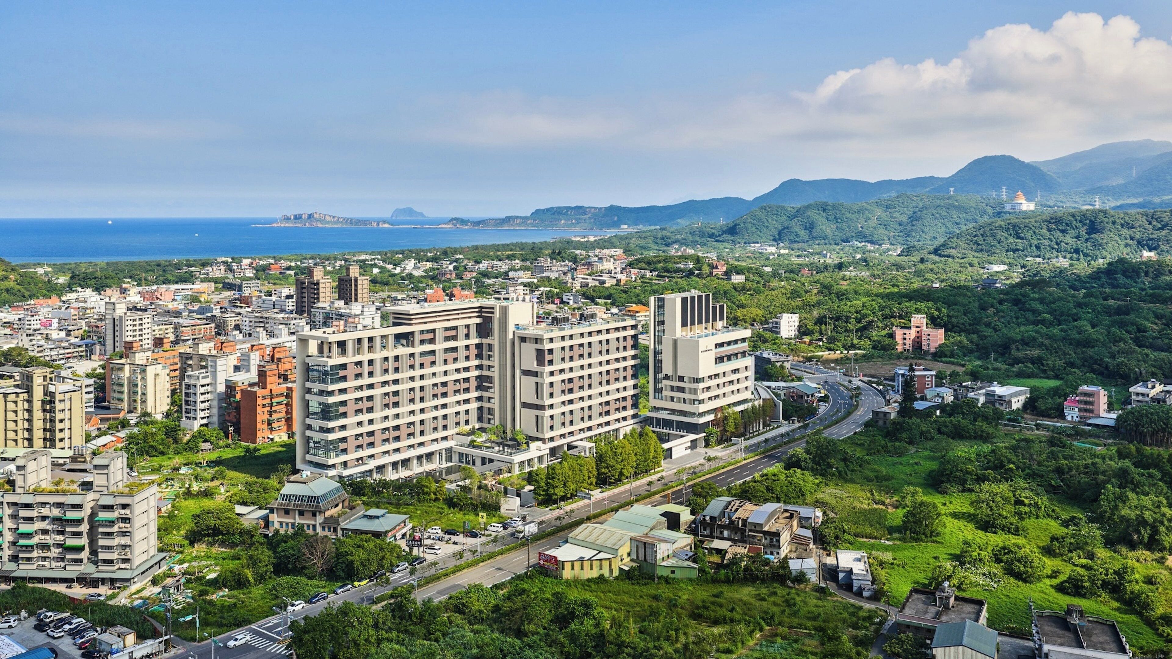 A high-rise building with multiple floors, surrounded by greenery and a coastal view.