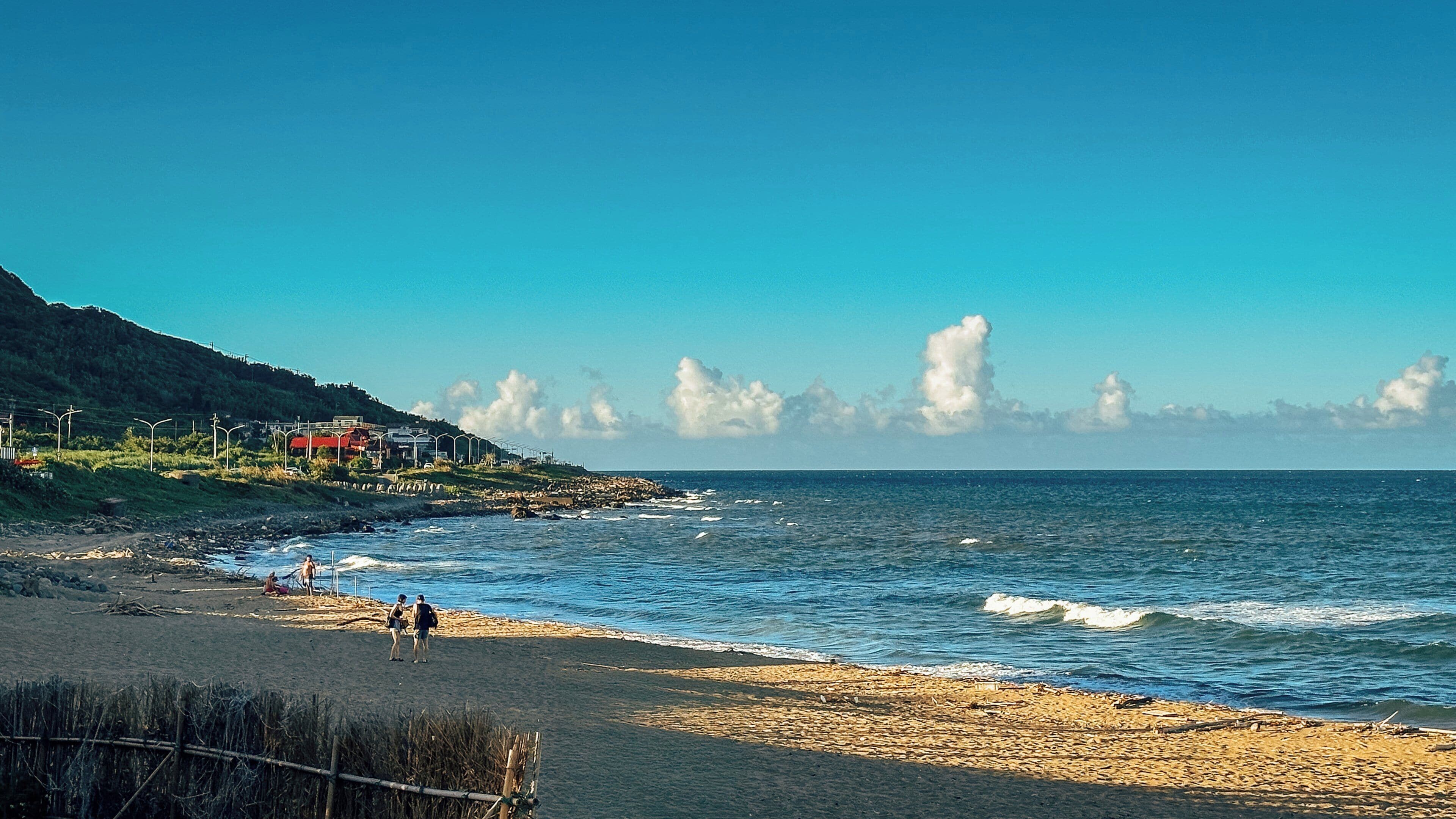 A beach with a rocky shoreline, a few people, and a clear sky.