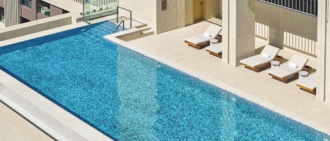 Una piscina con sillas de descanso y balaustrada de vidrio.