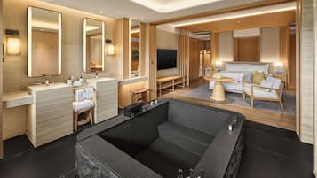 A modern hotel room with a large bathtub, a sofa, and a TV.