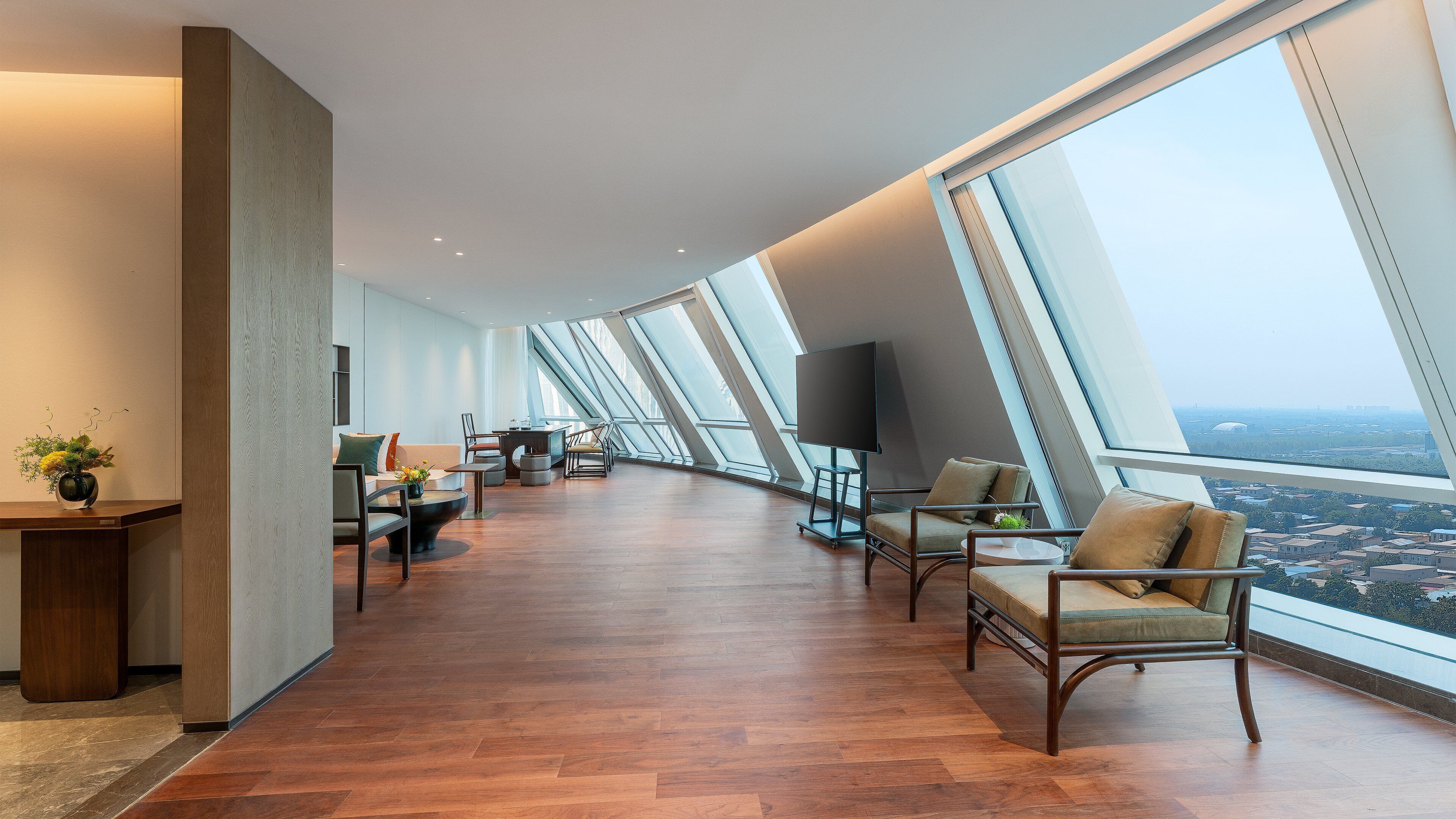A modern interior with a curved ceiling, large windows offering a city view, and a seating area with a small table and chairs.