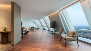 Een modern interieur met een gebogen plafond, grote ramen met uitzicht op de stad en een zithoek met een kleine tafel en stoelen.