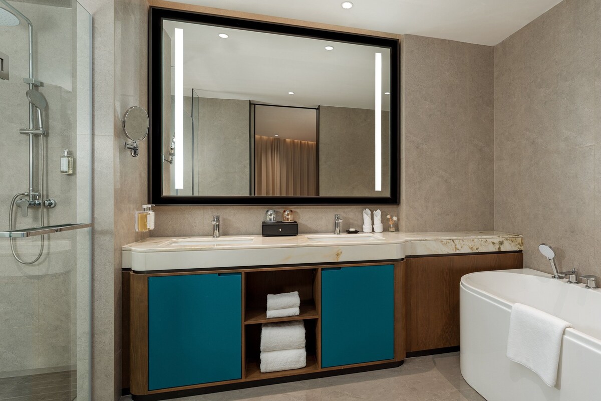 Un baño moderno con cabina de ducha de vidrio, un espejo grande, tocador con doble lavabo y una bañera independiente.