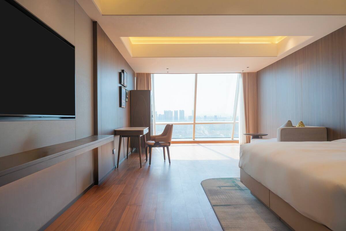 Een moderne hotelkamer met een groot bed, een bureau, een stoel, een flatscreen-televisie en een groot raam met uitzicht op de stad.