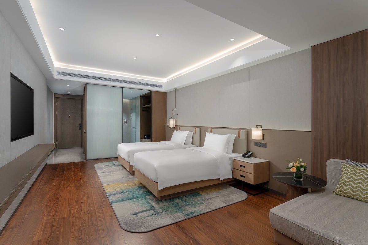 Een moderne hotelkamer met twee bedden, een bureau, een stoel, een televisie en een inloopkast.