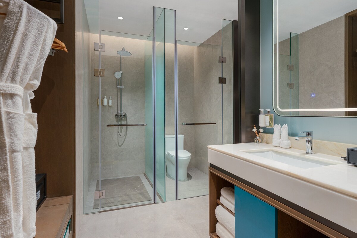 Un baño moderno con ducha acristalada, lavamanos blanco y un espejo grande.