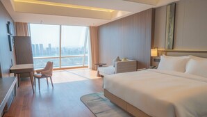 A hotel room with a large bed, a desk, a chair, a small table, and a view of the city. - Holiday Inn Xingtai Quancheng by IHG (Xingtai)