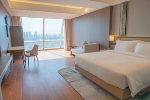 Habitación de hotel con una cama grande, un escritorio, una silla, una mesita y vista a la ciudad.
